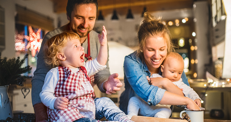 Mum, dad and two little children playing with flour while baking Christmas cakes