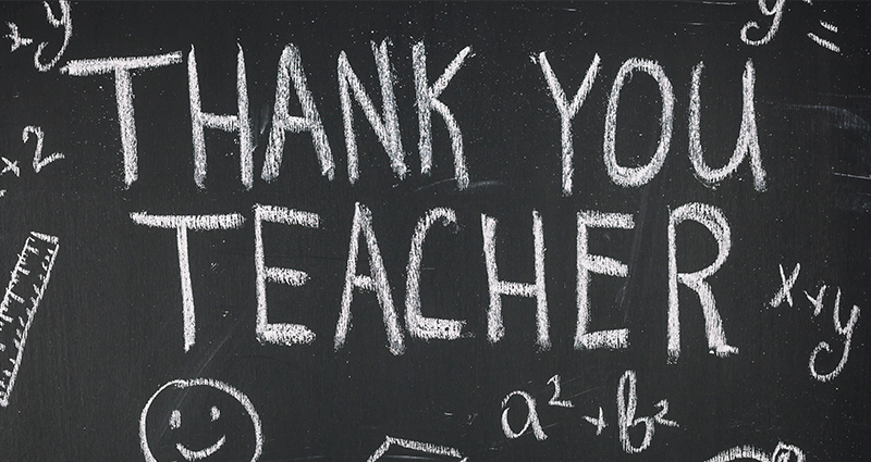 Nápis "Thank you Teacher" napísaný s kriedou na tabuľu, okolo nápisu detské kresby.
