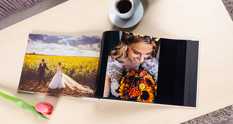 Open Starbook with wedding photos is laying on a light coffee table. A single, pink tulip and a cup of coffee are laying close.