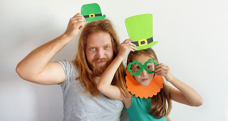 Un padre e sua figlia con in mano dei cappelli verdi di cartone, che guardano verso l'obiettivo.