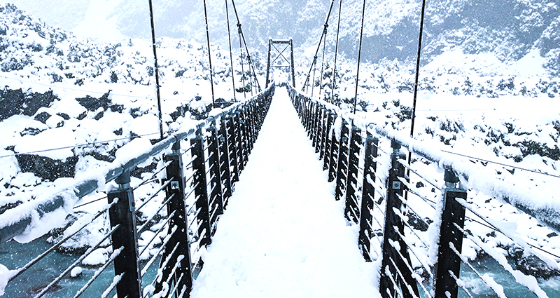 Foto von Samuel Scrimshaw von Unsplash -  eine schneebedeckte Brücke und das Gebirge im Hintergrund