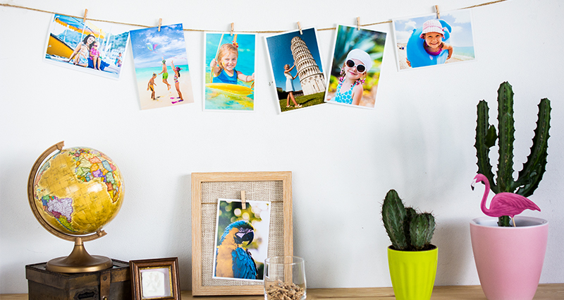 Die Sommerfotoabzüge, die Bilder an einer Schnur, links ein Globus auf einer hölzernen Schatulle, rechts zwei Kakteen in bunten Blumentöpfen.