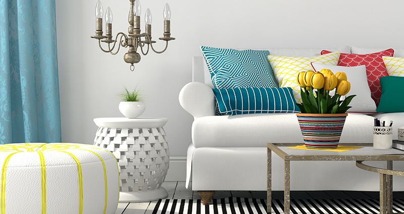 Picture of a bright living room with colourful decorations (cushions, a pouf, curtains and a rug) in various patterns.