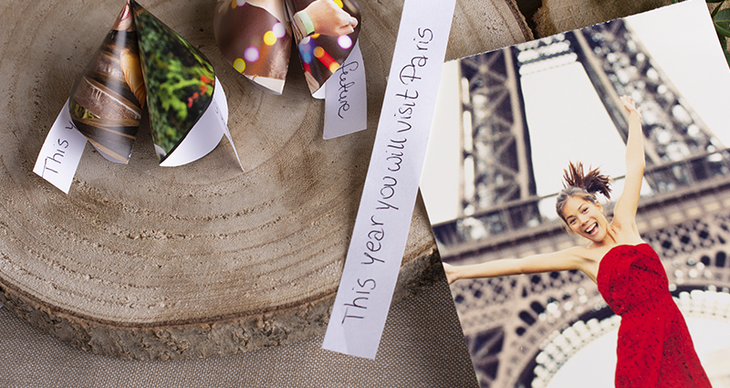 Close-up on a chinese cookies made of prints on a wooden discs, a note with the fortune caption 'This year you will visit Paris' and a print that shows a happy woman next to the Eiffel Tower 