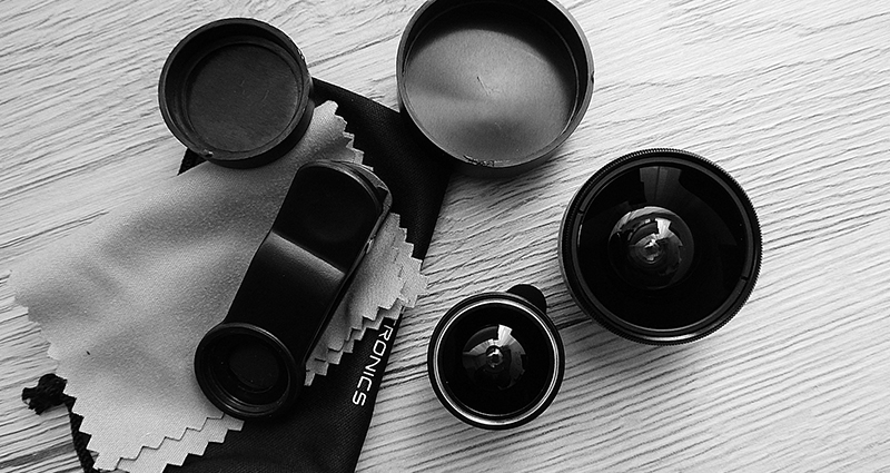 Set of phone or tablet lenses lying next to a micro-fibre cloth and a case – a black and white photograph