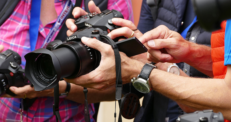 Trys žmonės žiūri savo nuotraukas ant fotoaparatų ekranų.