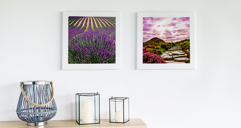 Two landscape photo canvases on the wall above a bookshelf with 3 candlesticks