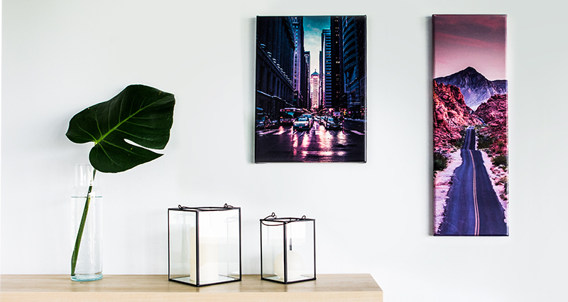 Deux nouveaux formats des toiles photo sur un mur au-dessus d’une étagèrere et une feuille de monstera dans un flacon.