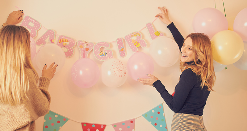 Two women decorating the wall for a baby shower