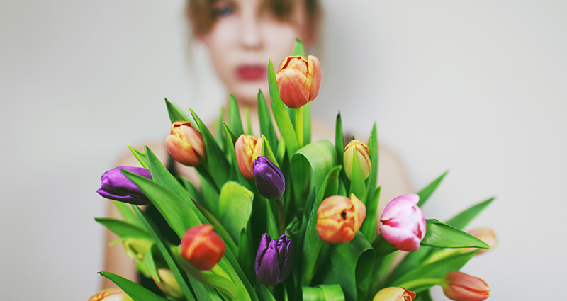 Woman holding a bucket of tulips, blurred figure in the background.