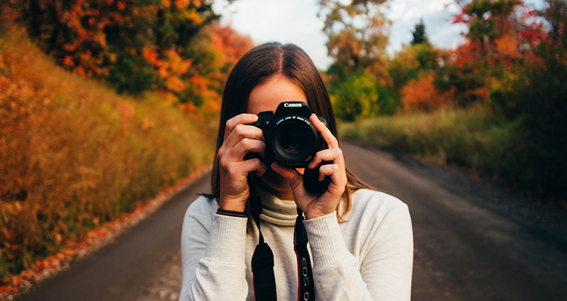 Woman taking a picture facing a photograph, colourful leaves in the background