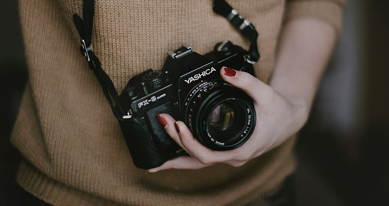 Donna che indossa un maglione marrone e tiene una macchina fotografica