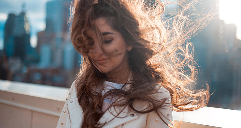 Una donna con i capelli arruffati, con degli edifici sullo sfono