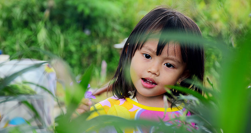Foto de una niña entre las hojas.