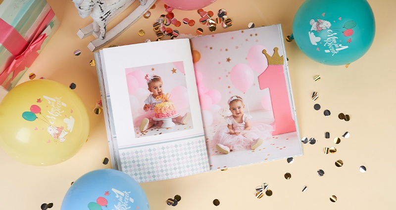 Une idée cadeau pour un enfant d'un an - un livre photo avec des photos du premier anniversaire d'une fille, entourés par des ballons et des confettis.