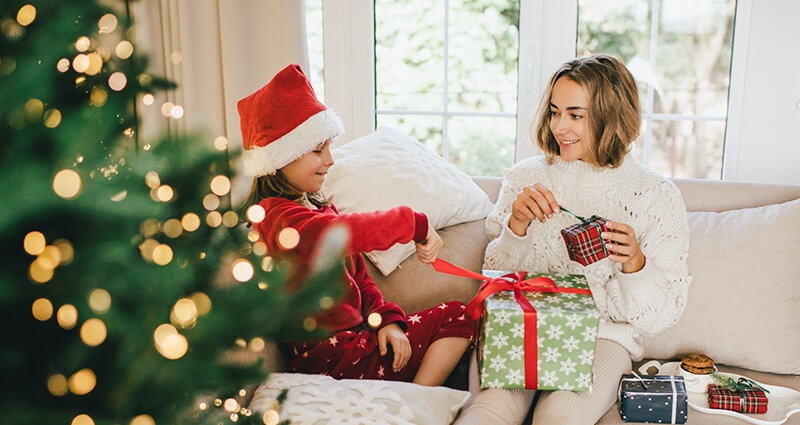 Matka s dcerou otevírají dárky a čtou novoroční přání napsaná na lístečku.