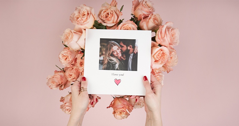 Žena drží otvorenú fotoknihu s fotografiami na pozadí ruží. 