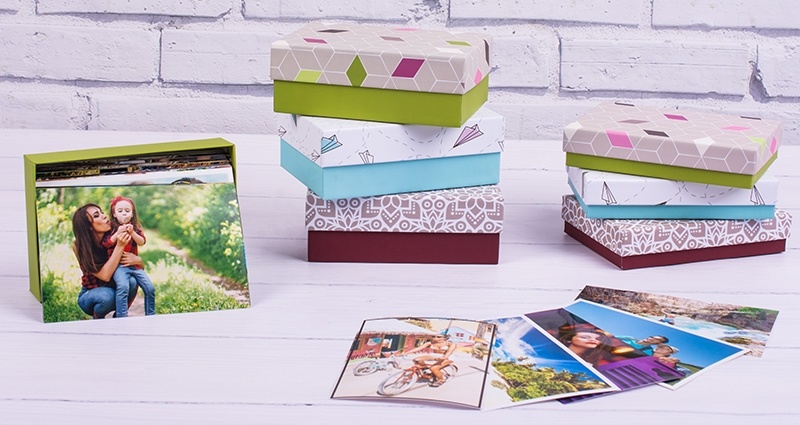 Collection of big and small boxes for photo prints lying on the table, next to them spread prints; the wall of bricks in the background.