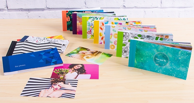 Sammlung von Sharebooks mit neuen Covern auf einem Schreibtisch. Ein Teil der Sharebooks steht auf der rechten Seite in einer Reihe, der andere Teil liegt auf der linken Seite. 3 Fotos lose in der Mitte des Schreibtisches, im Hintergrund eine Ziegelmauer.