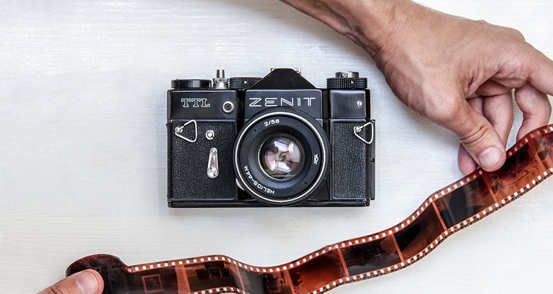Inzoomen op de handen van een man en op een fotorolletje; in het centrale deel van deze foto – een analoge camera. 