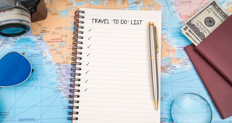 Un cuaderno espiral, al lado del pasaporte, del dinero, de la cámara y de las gafas de sol, en el fondo un mapa colorido.
