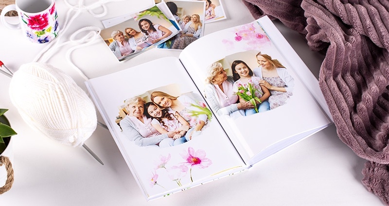 Un livre photo et des tirages qui présentent une grand-mère avec ses petits enfants, à côté un mug photo, une couverture et un pot de thé.