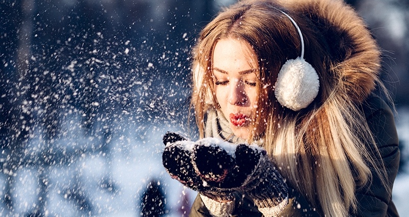 Eine junge Frau bläst eine Handvoll Schnee