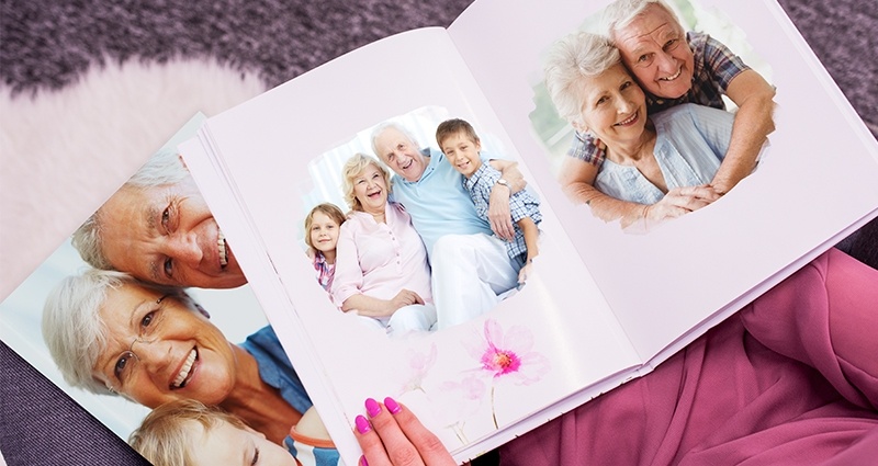 Une femme habillée en rose assise dans un fauteuil gris regardant un livre avec des photos de famille. Sur ses genoux un deuxième livre photo - vue du vol d’oiseau.